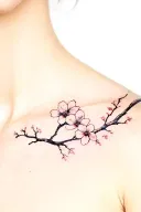 A fine-line, realistic cherry blossom tattoo placed centrally between the collarbones. The blossom has delicate black in tattoo design idea